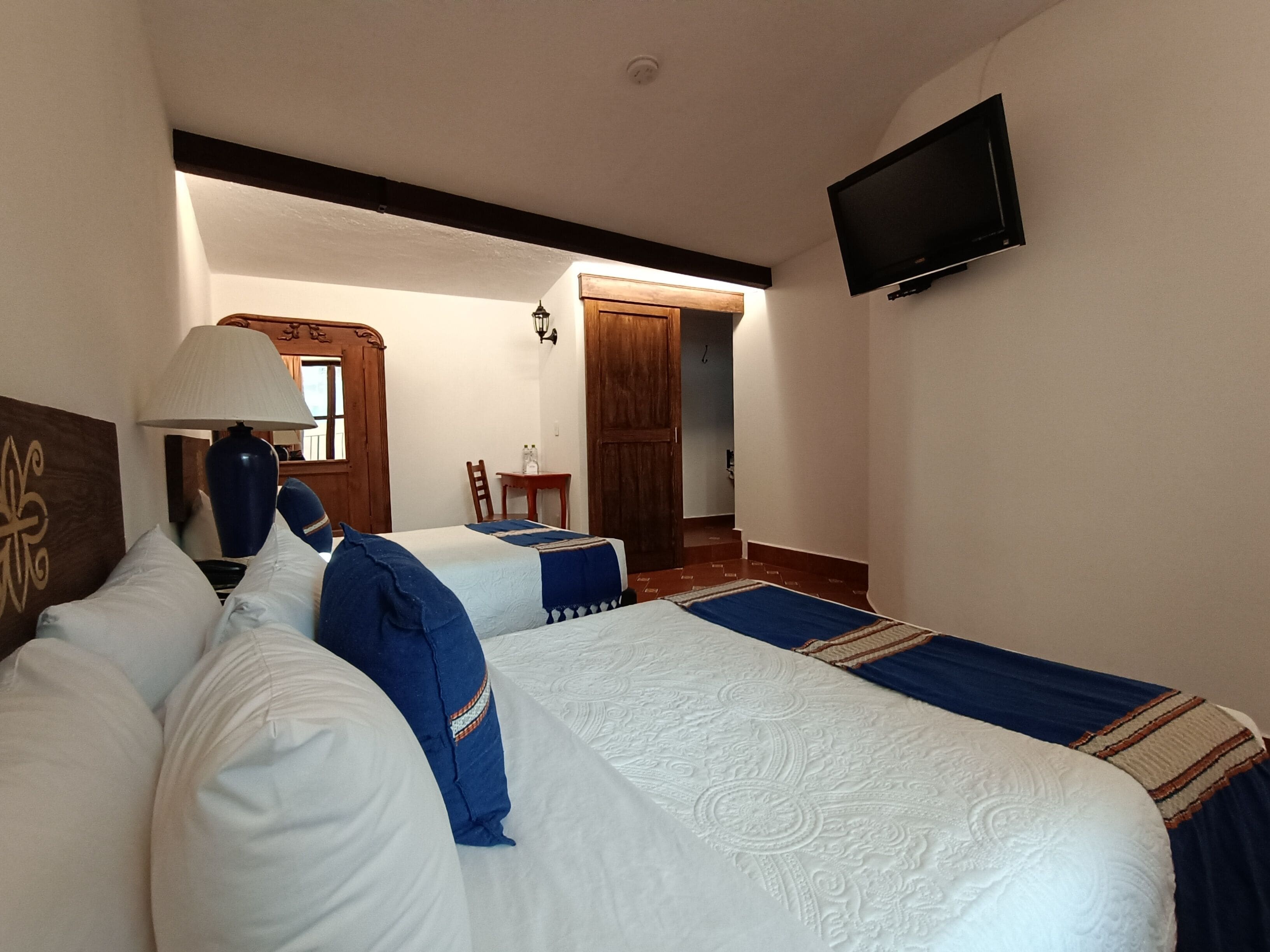 A hotel room with two beds, a TV, a lamp, and a wooden door.