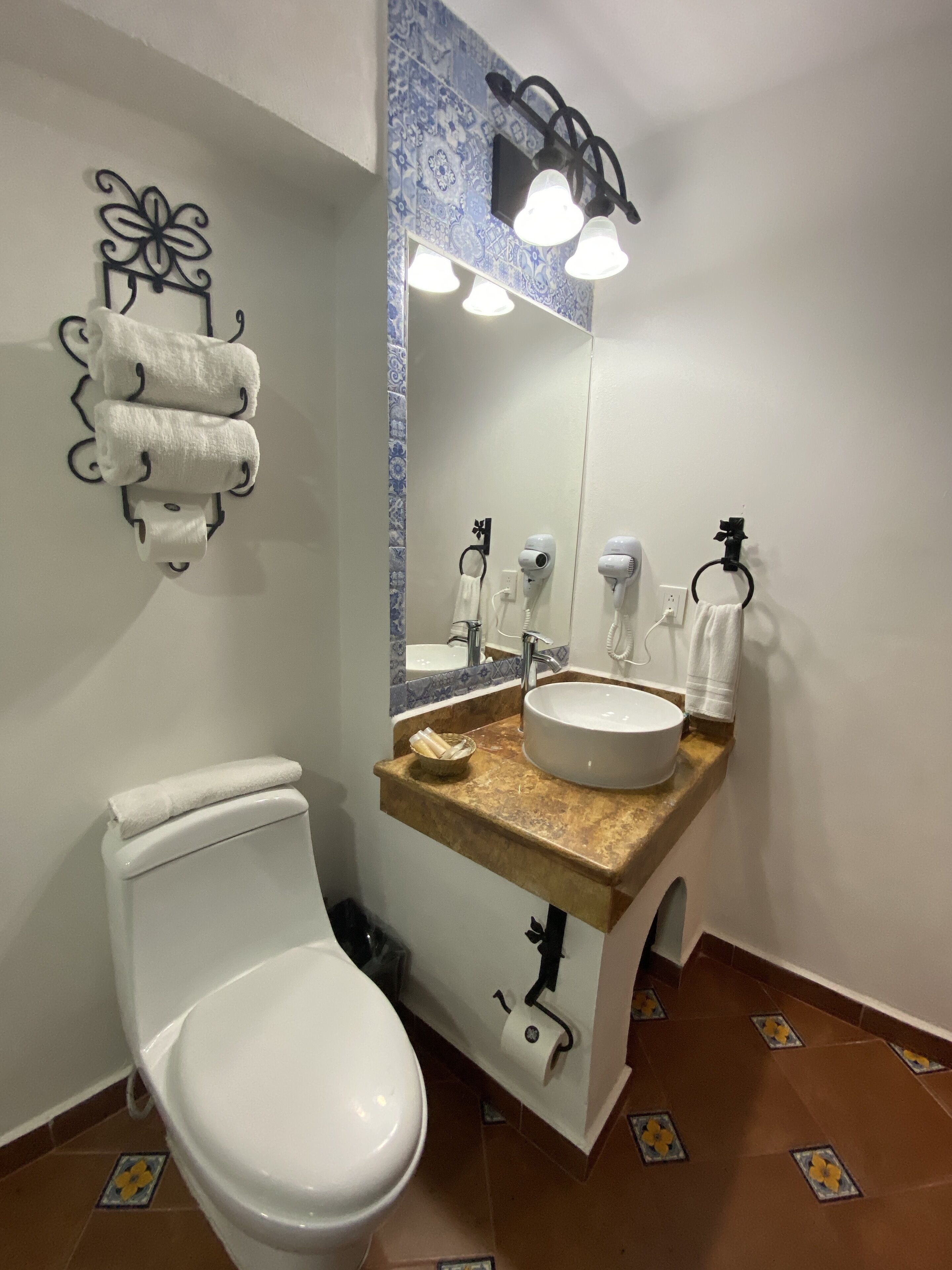 Un baño con inodoro blanco, un lavabo con espejo encima y un perchero con toallas.