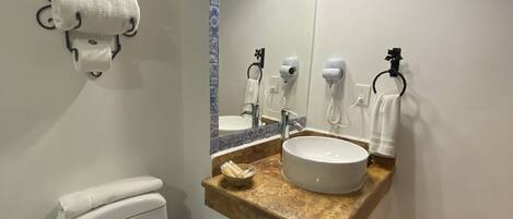 Un baño con inodoro blanco, un lavabo con espejo encima y un perchero con toallas.