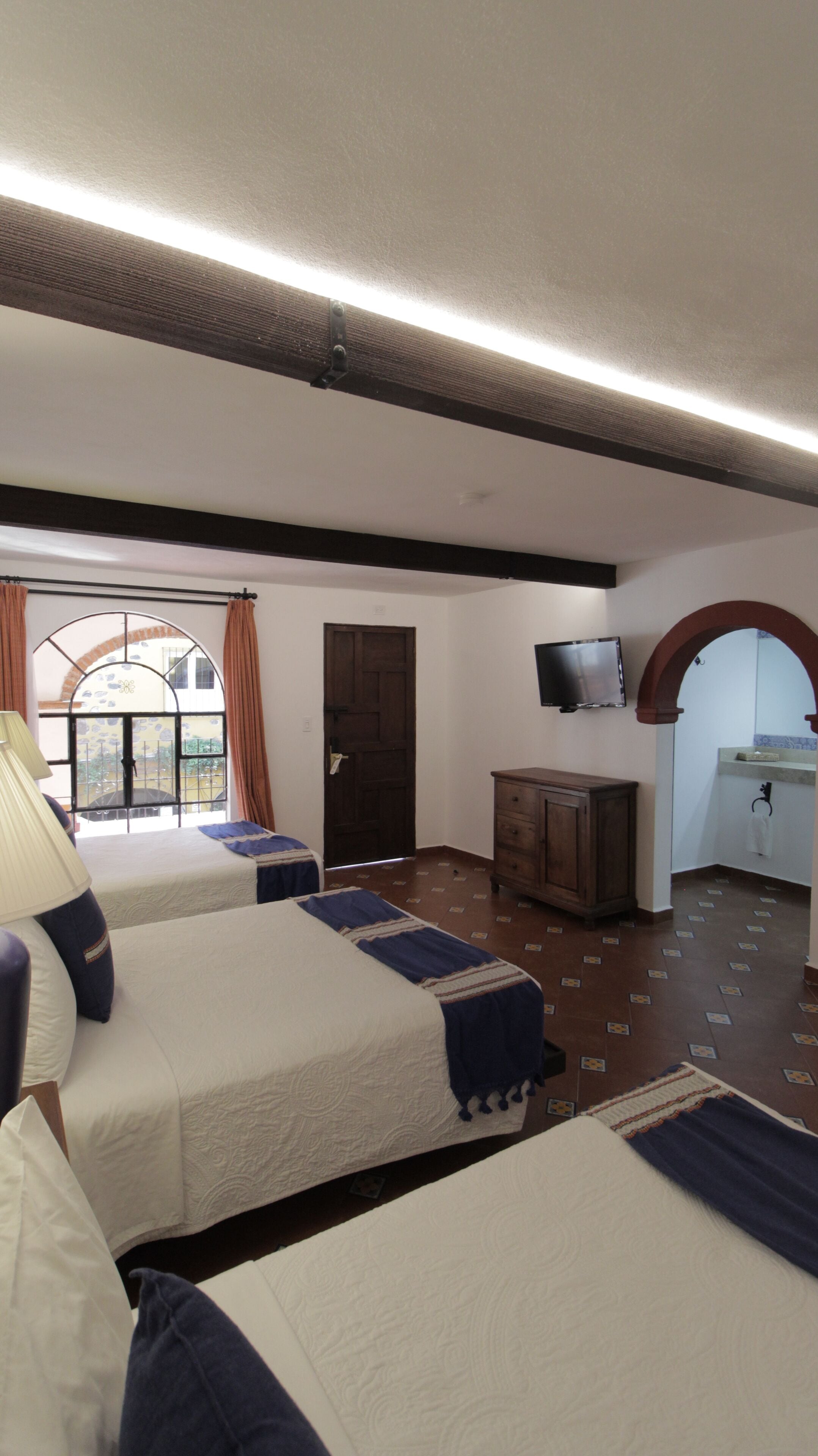 Habitación de hotel con dos camas, televisión, un aparador de madera y baño con espejo y lavabo.