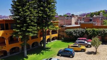 A parking area with several cars, a large tree, and a building with yellow walls and balconies.