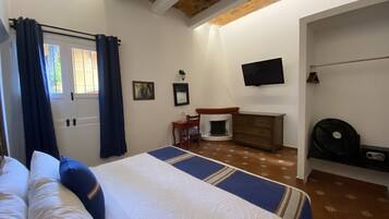 A bedroom with a bed, a dresser, a television, and a fireplace.