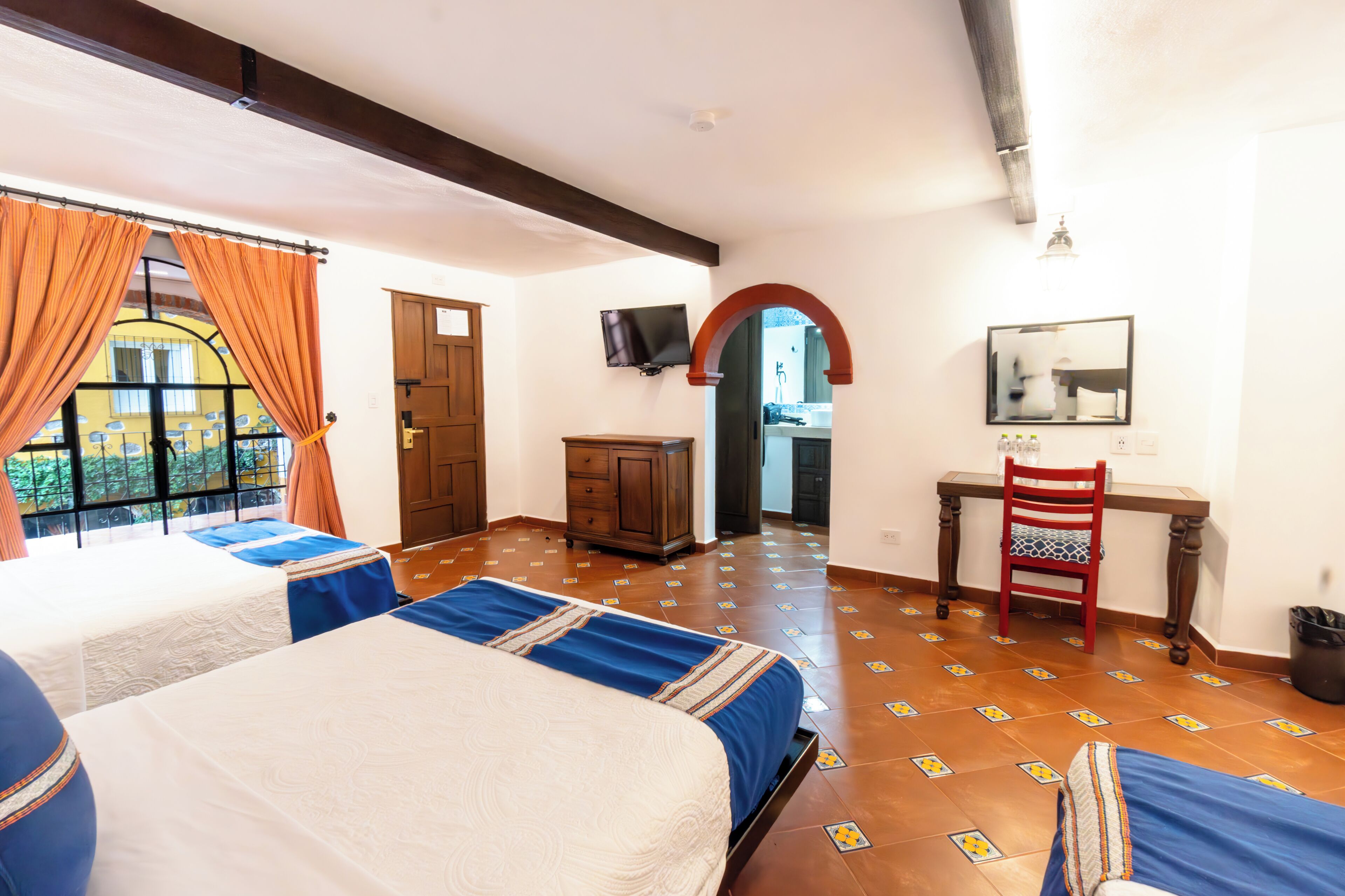 A hotel room with two beds, a desk, a chair, and a TV.
