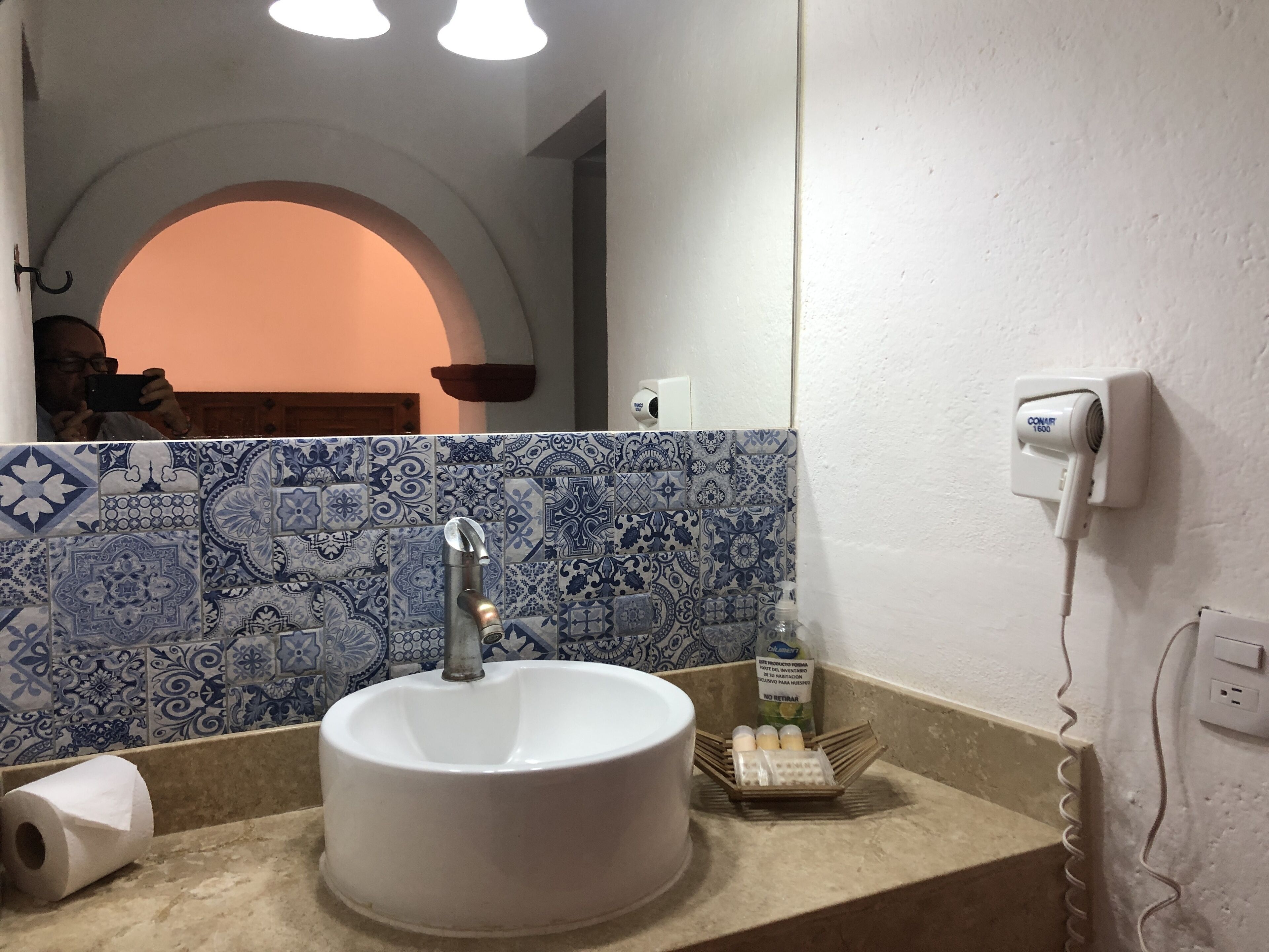 A bathroom with a white sink, blue patterned tiles, a mirror, and a hairdryer on the wall.