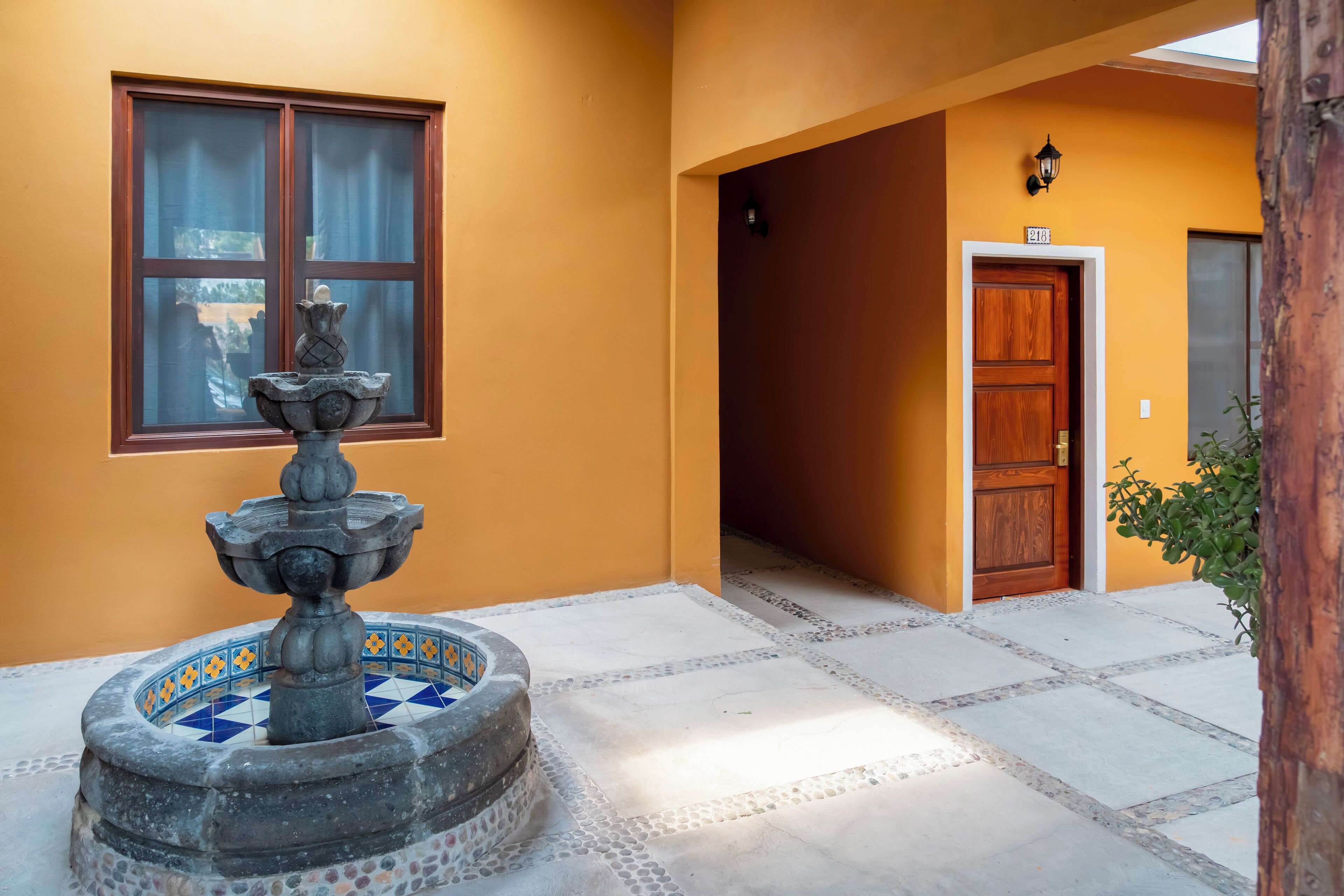 A courtyard with a stone fountain, a window with curtains, and a wooden door.