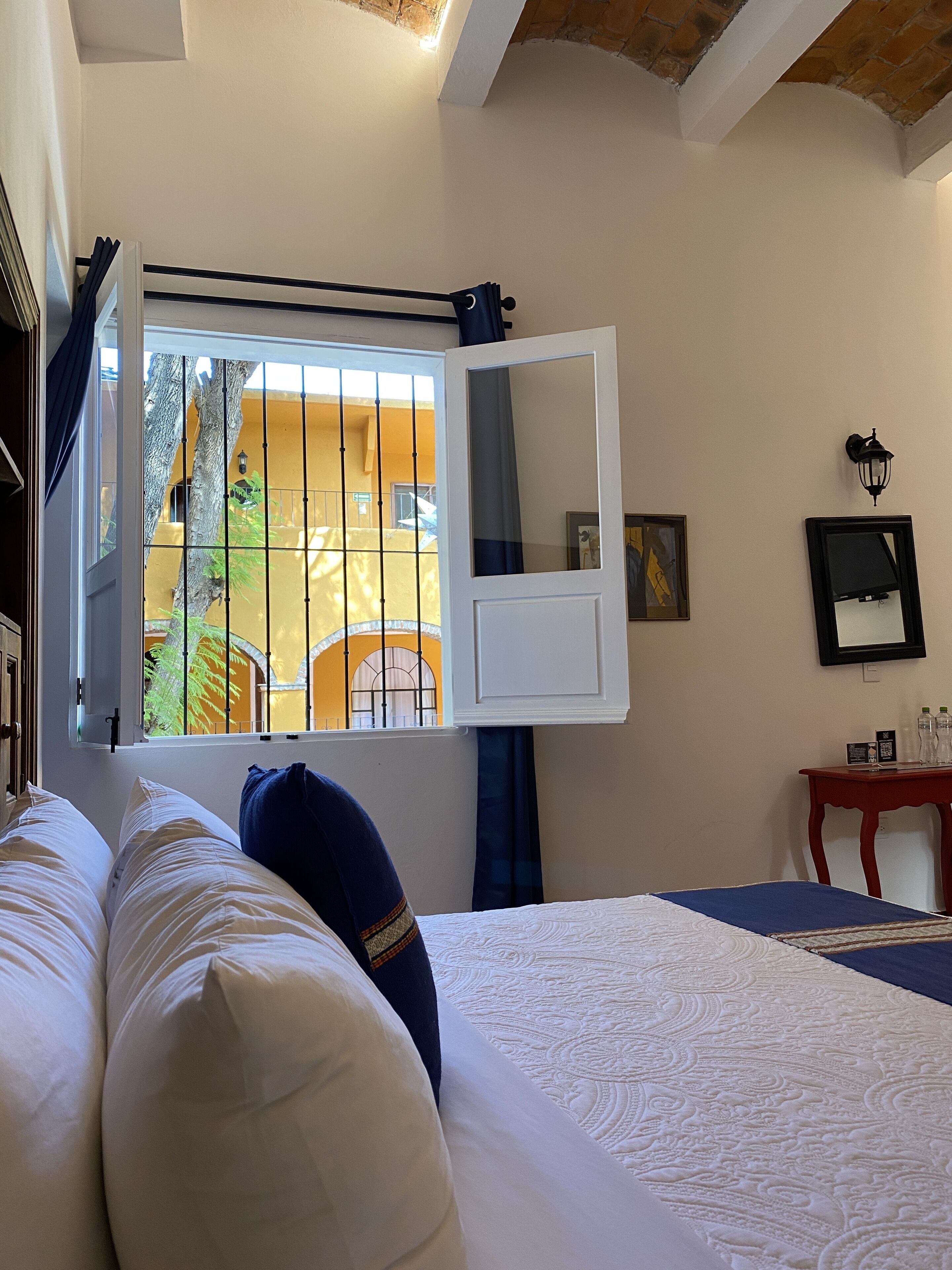 Un dormitorio con cama, ventana con cortinas, mesita de noche y lámpara de pared.