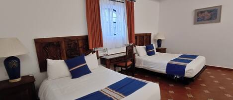 Habitación de hotel con dos camas, cabecero de madera, escritorio, silla, lámpara y un cuadro en la pared.