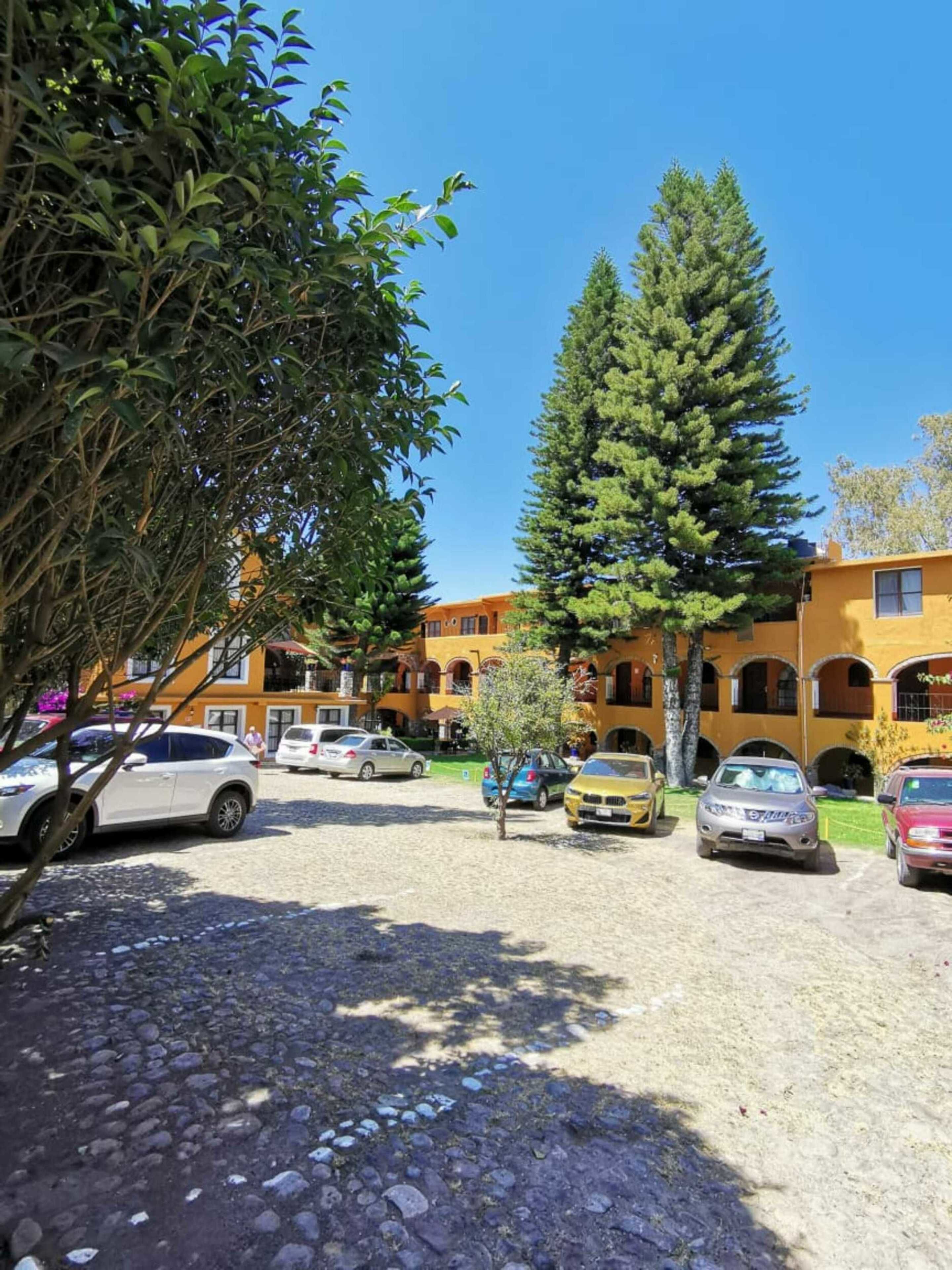 Un hotel con estacionamiento en un patio interior, rodeado de árboles y edificios con fachadas amarillas y anaranjadas.