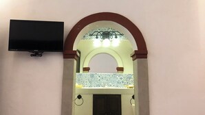 Une pièce dotée d’un sol carrelé, d’un téléviseur à écran plat fixé au mur et d’une porte en arc donnant sur une autre pièce.