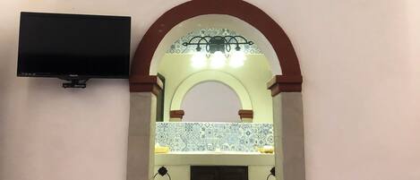 A room with a tiled floor, a flat-screen TV mounted on the wall, and an arched doorway leading to another room.