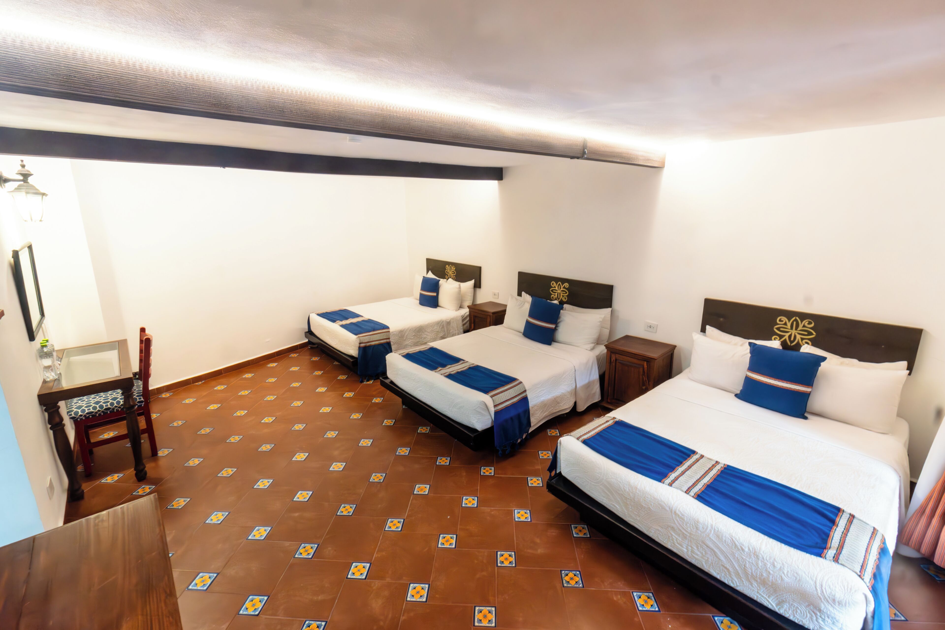 Una habitación de hotel con tres camas individuales, una silla de madera y suelo de baldosas.