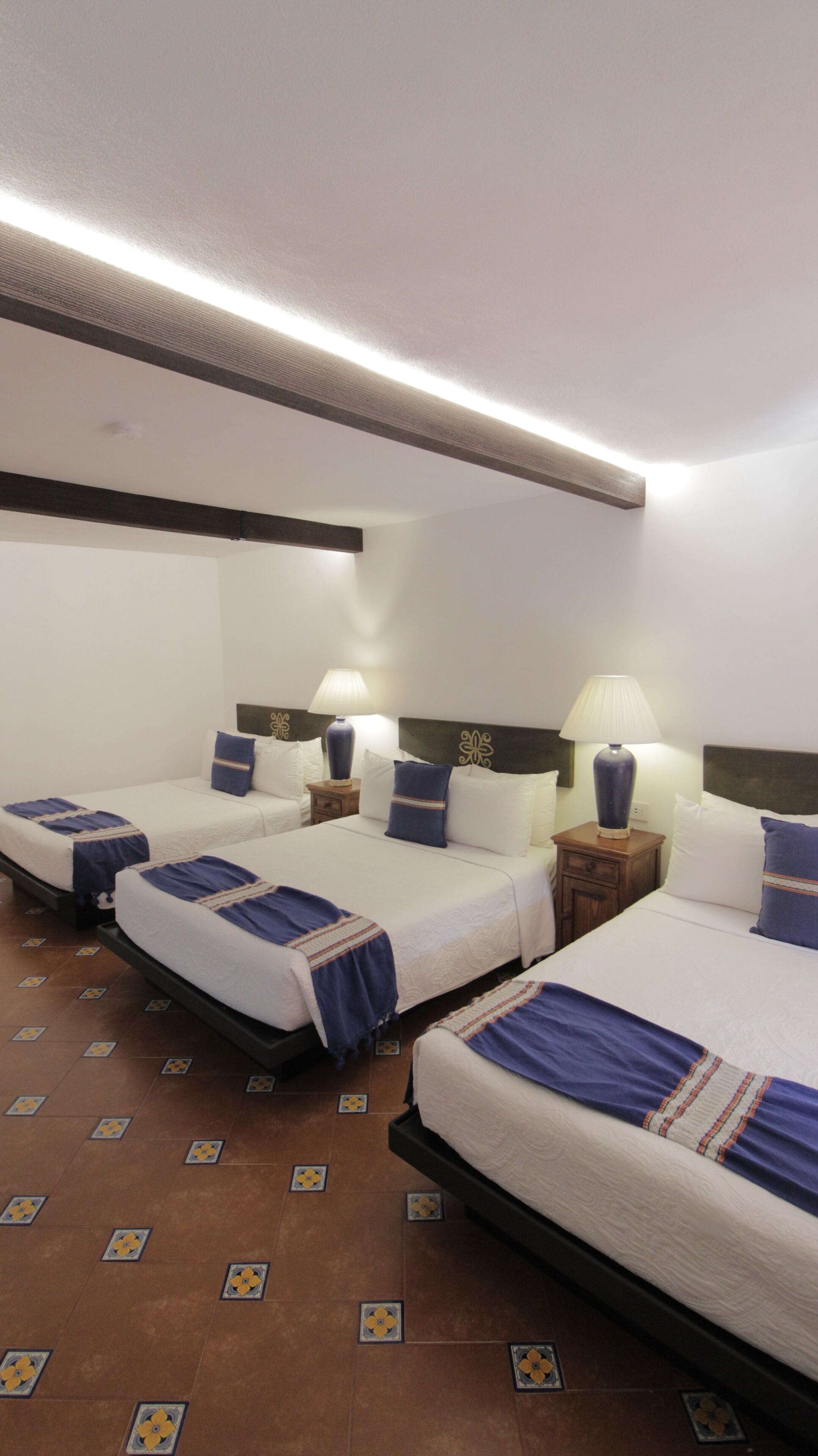 A hotel room with two beds, each with a blue and white bedspread, two bedside tables with lamps, and a patterned floor.