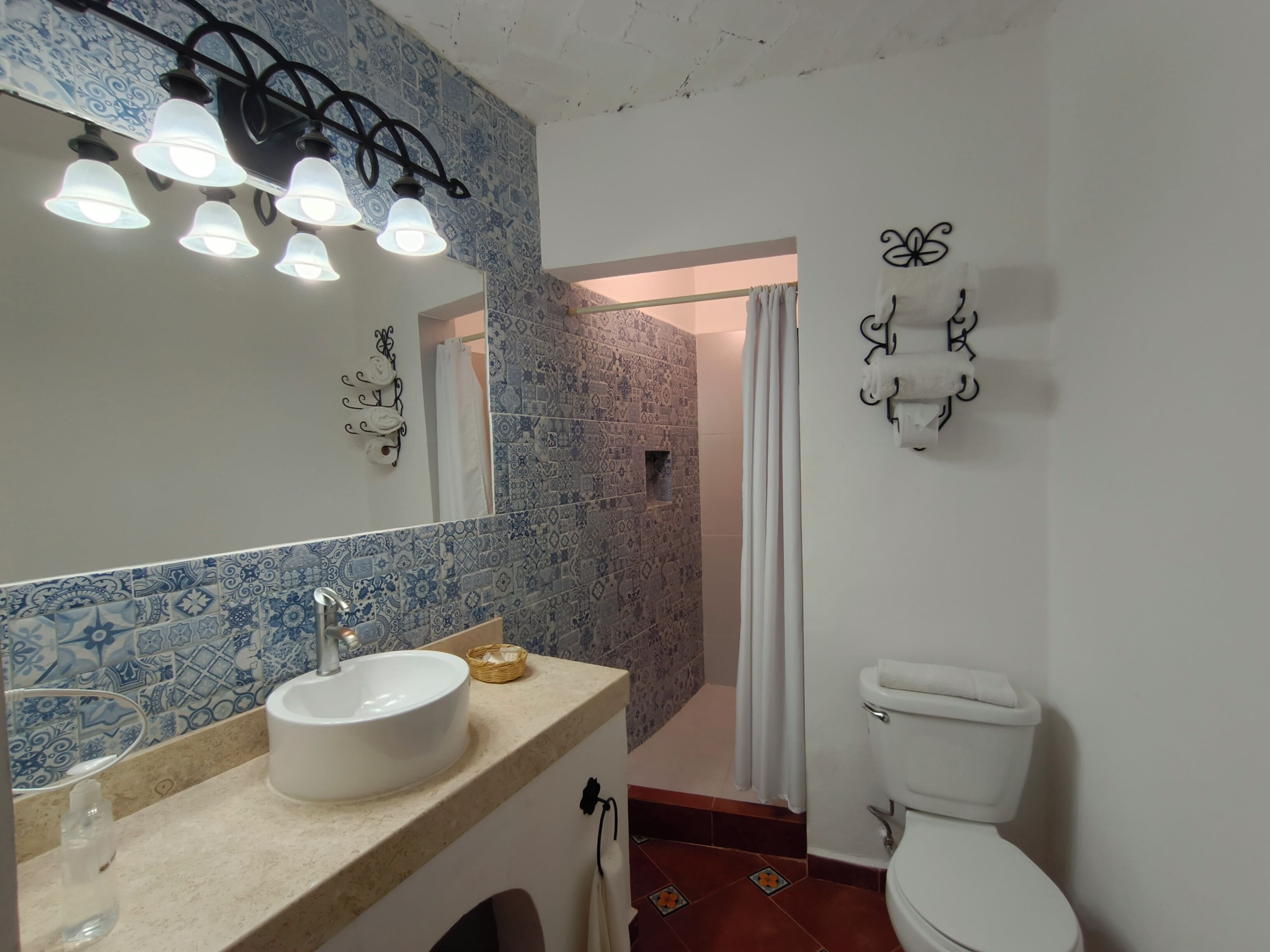 A bathroom with a white sink, a mirror, and a toilet. There is a shower curtain and a towel rack.