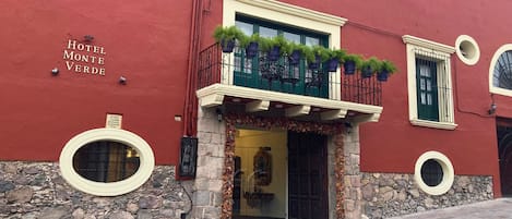 Um edifício vermelho com base de pedra, uma varanda com plantas em vasos e uma placa com o dizer
