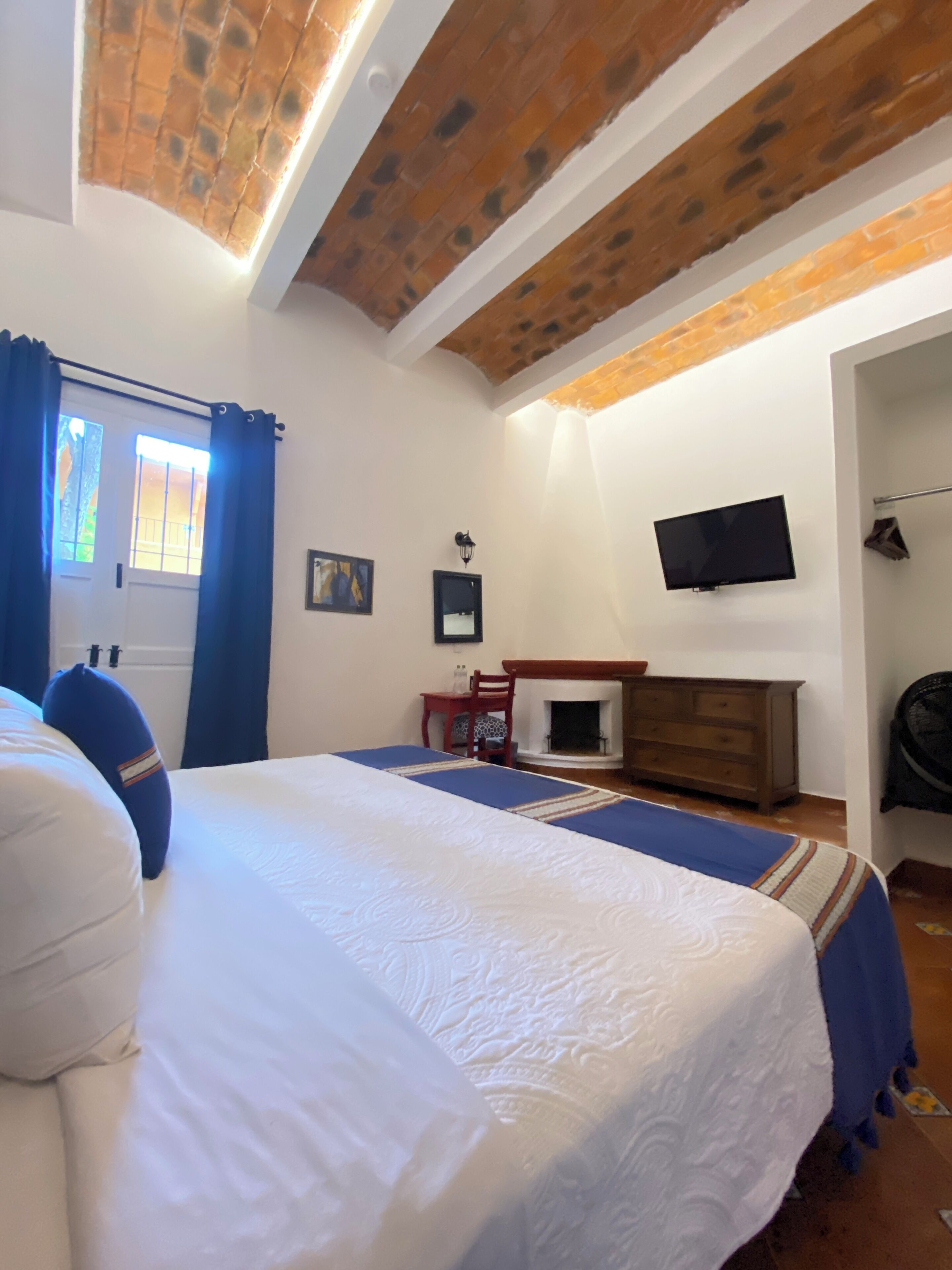 A bedroom with a large bed, a television on the wall, and a fireplace.