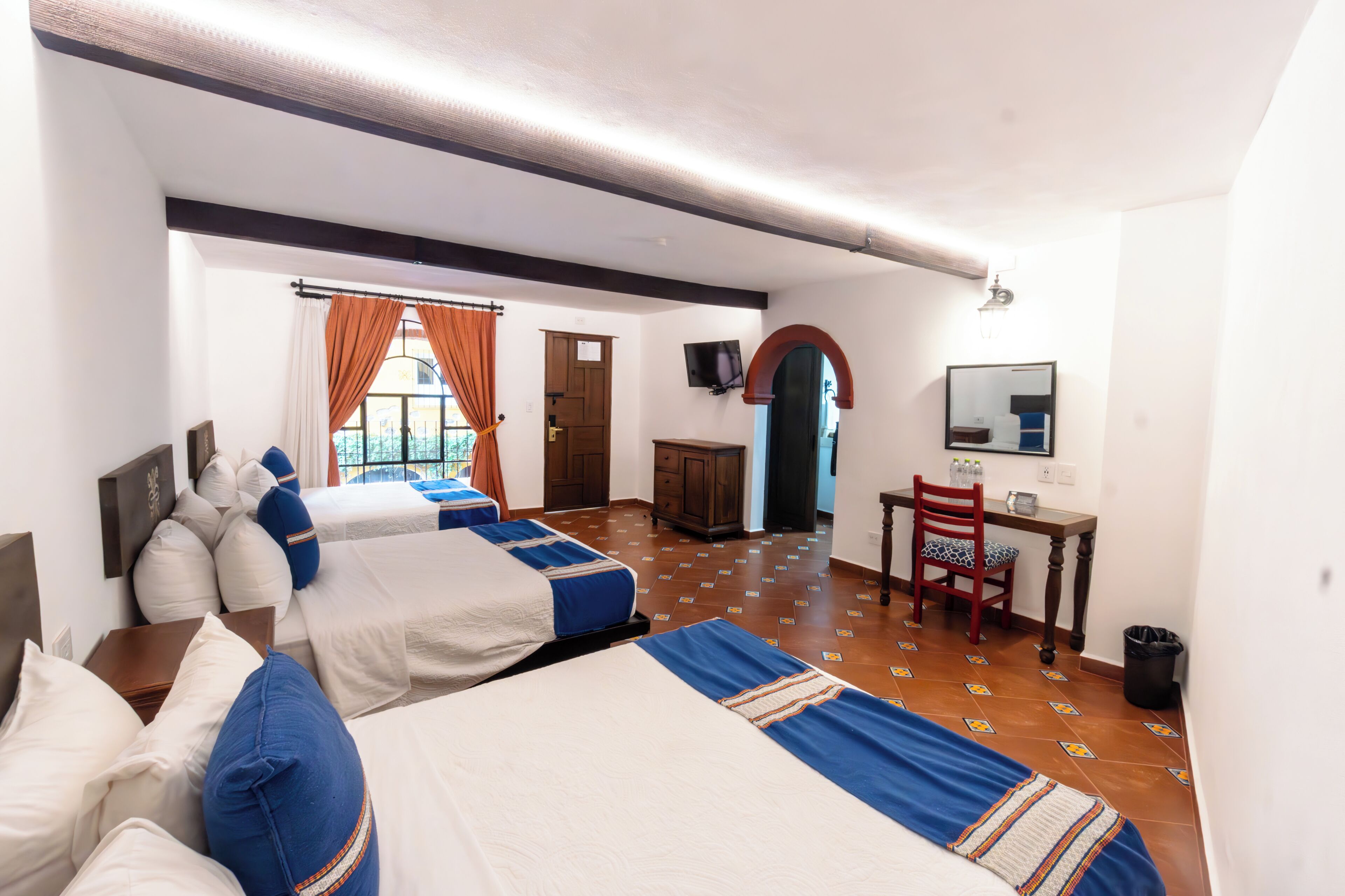 A hotel room with three beds, a desk, a chair, a television, and a mirror.