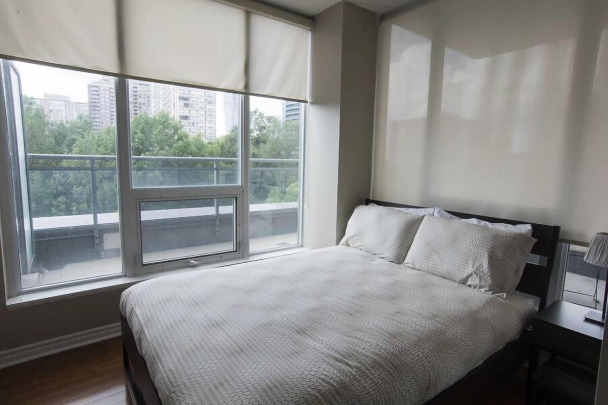 A bedroom with a large window, a bed, and a nightstand.