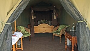 Una habitación con carpa, una cama de madera, dos sillas, una mesita y un espejo.