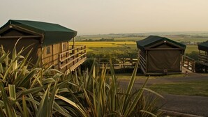 Vista de una zona rural con dos cabañas pequeñas de techo verde, rodeadas de campos y una lejana perspectiva de un valle.