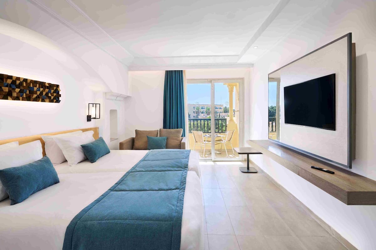 A hotel room with a large bed, a TV mounted on the wall, and a balcony with a view of the city.