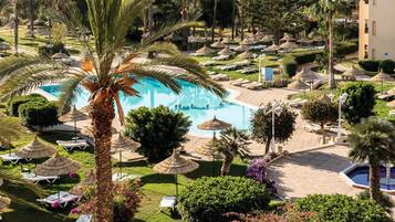 Un resort con piscina rodeada de sillones de descanso y palmeras.