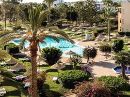 Un resort con piscina rodeada de sillones de descanso y palmeras.