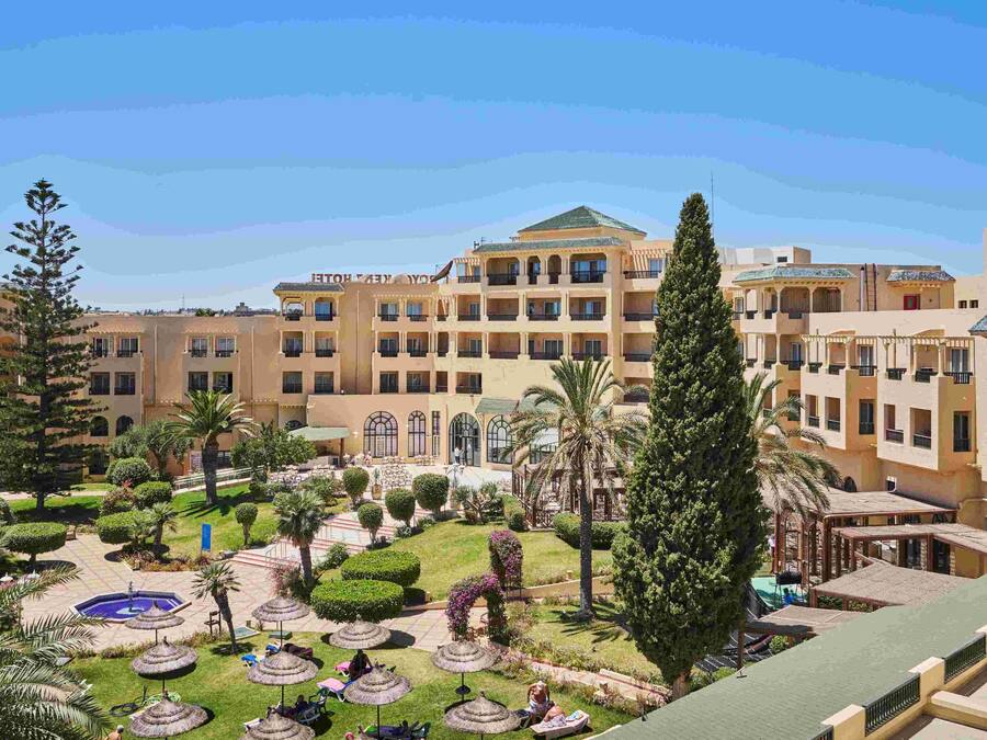 Un patio de hotel con piscina, palmeras y una fuente central.