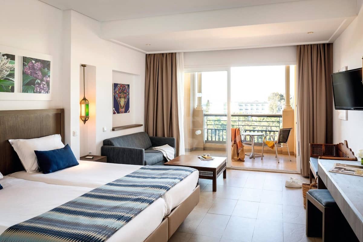 A hotel room with a large bed, a sofa, a desk, and a balcony with a view.