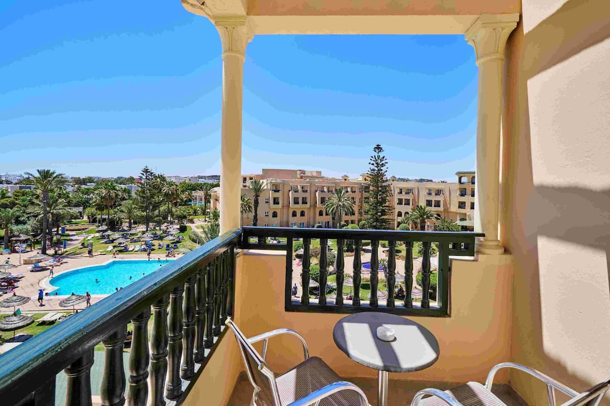 A balcony with a pool view, outdoor seating, and a view of a hotel complex.