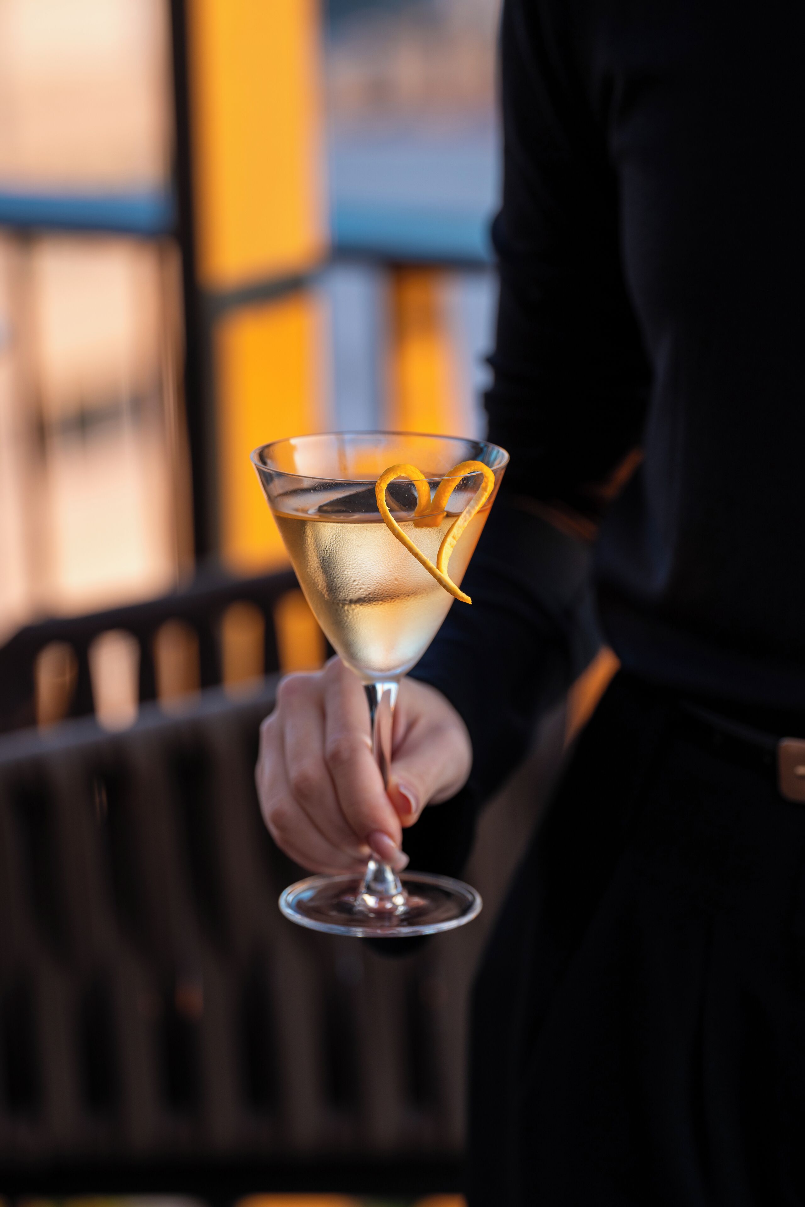 Iemand houdt een martini glas vast met een citroen twist.