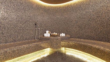 Une salle de spa aux murs et au sol recouverts de mosaïques, avec un coin salon et un petit autel agrémenté de bougies et d’un récipient.