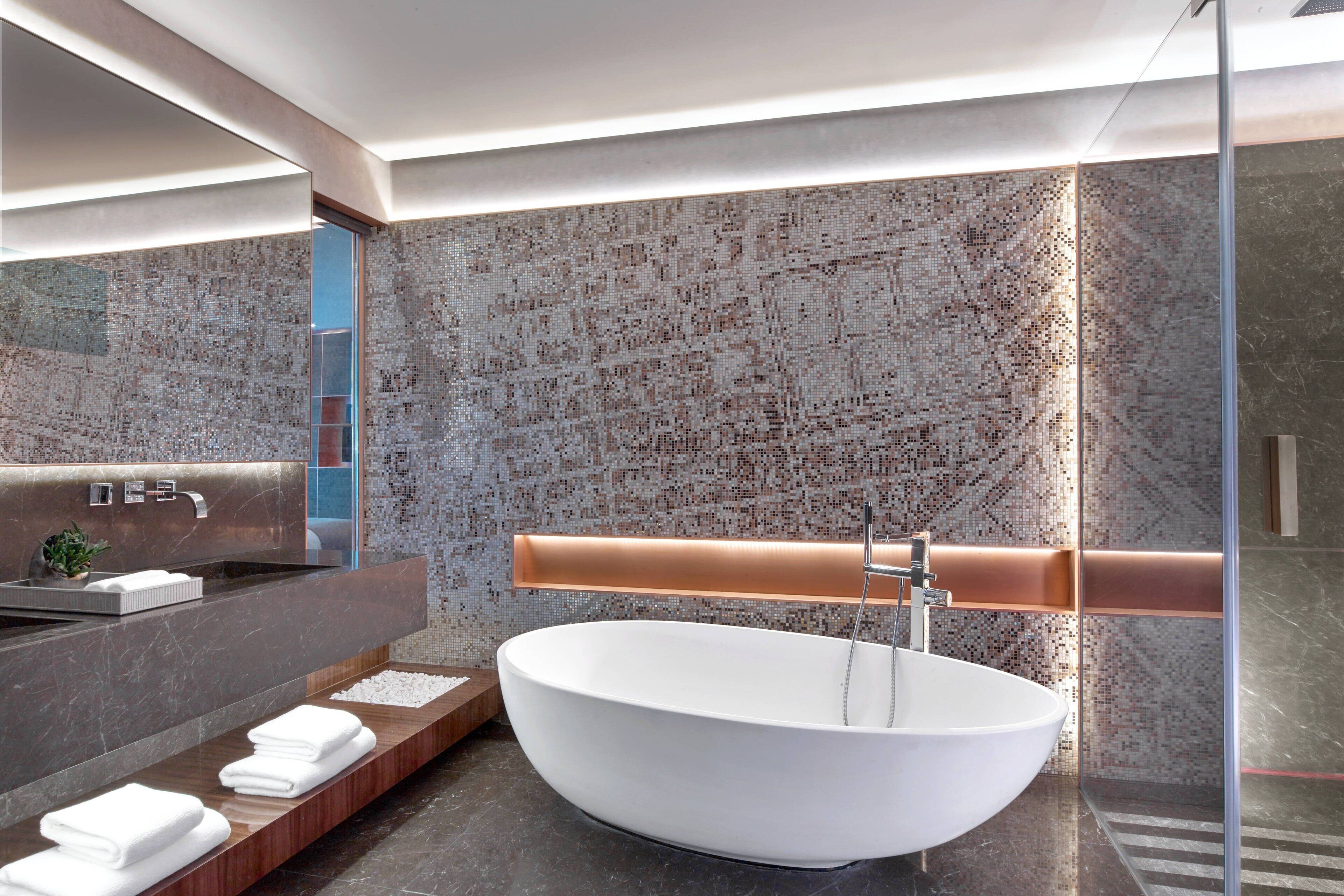 Une salle de bain moderne avec une baignoire sur pieds, un grand miroir et un pare-baignoire en marbre.