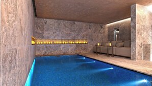 A modern indoor pool with a clear blue water surface, a seating area with sofas and a small table, and a wall-mounted light fixture. - The St. Regis Istanbul (Istanbul)