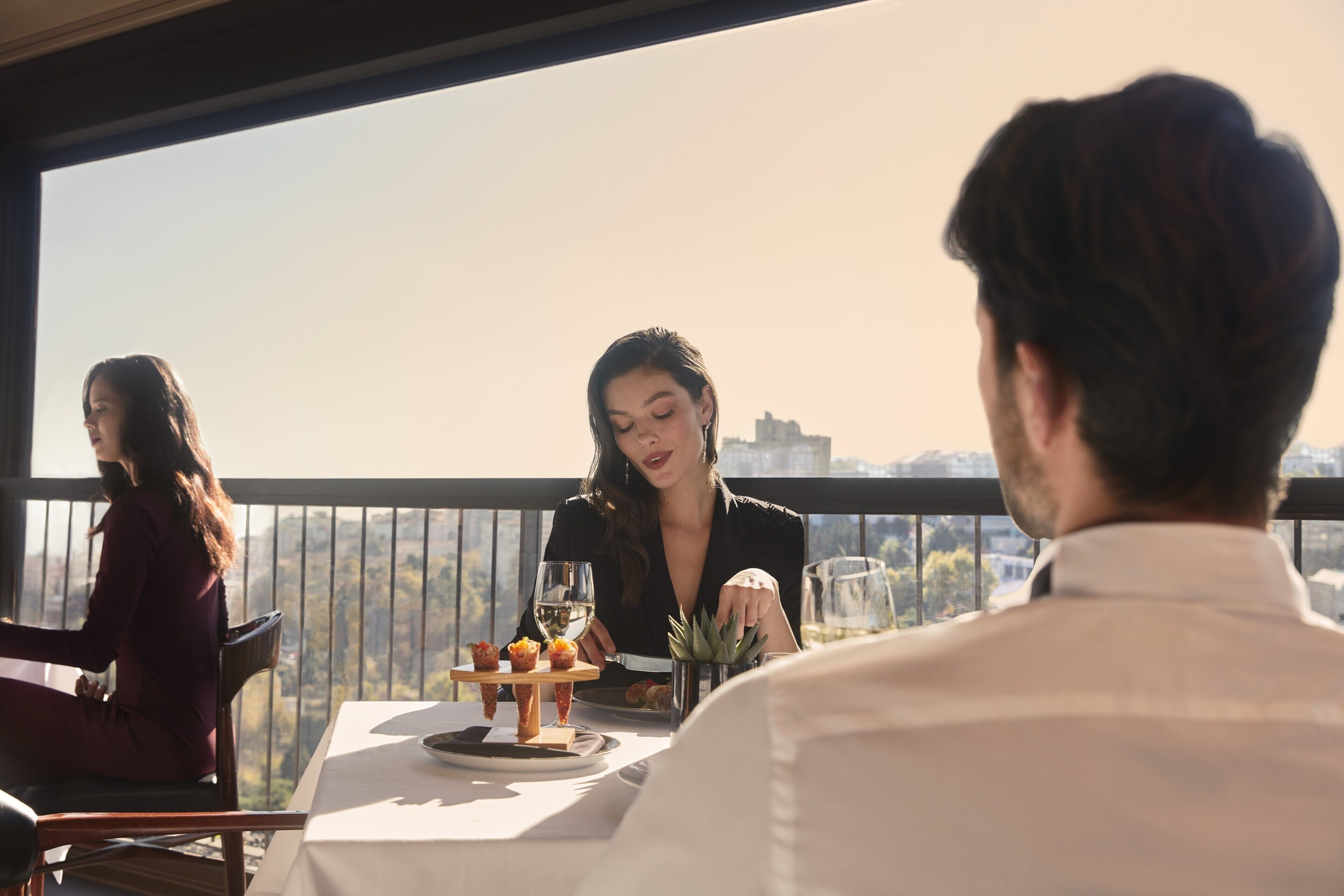 A dining area with a table set for three people, a city view, and a balcony railing.