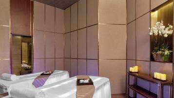 A spa room with two massage tables, a wooden console table with candles, and a large mirror on the wall.