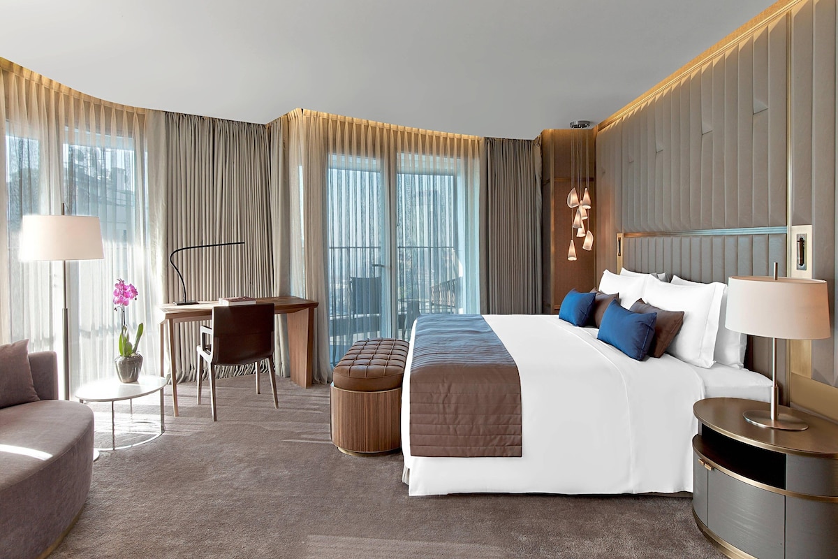 A modern hotel room with a large bed, a desk, a chair, and a sofa.
