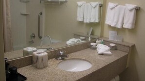 Un baño de hotel con lavabo, espejo, toallero y zona de ducha.