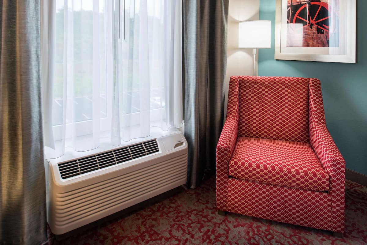 A room with a window, a red patterned chair, a wall-mounted lamp, and a framed picture.