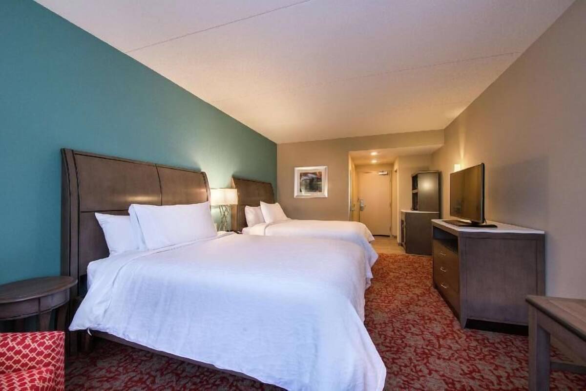 A hotel room with two beds, a desk, a TV, and a small table.