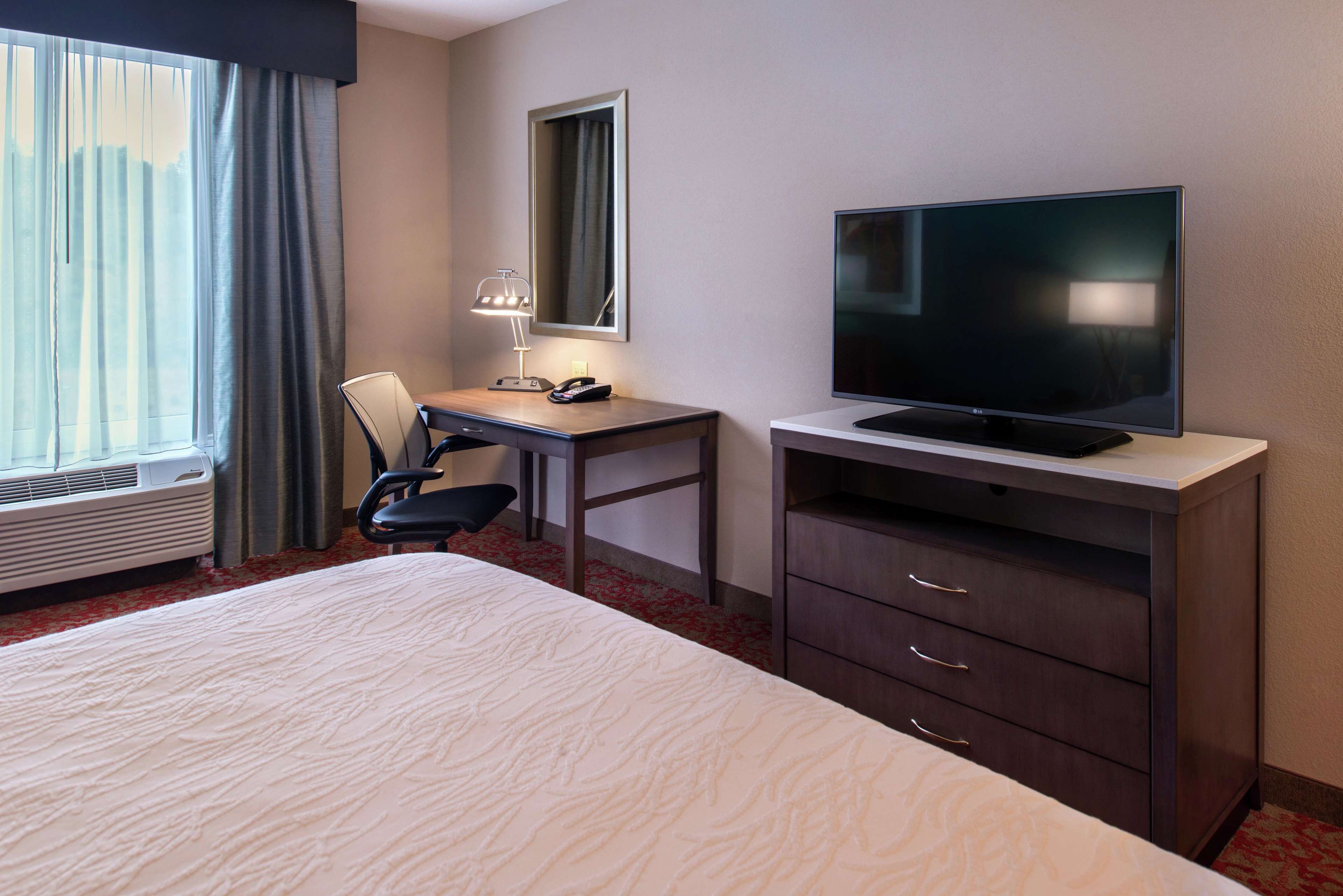 Une chambre d’hôtel avec un lit, un bureau doté d’une lampe, une télévision et une chaise.