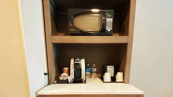 Una kitchenette compacta con microondas, cafetera y refrigerador.