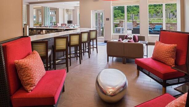 A modern hotel lobby with a bar area, seating with red upholstered sofas, and large windows offering views of the outdoors. - Hilton Garden Inn Bristol (Bristol)