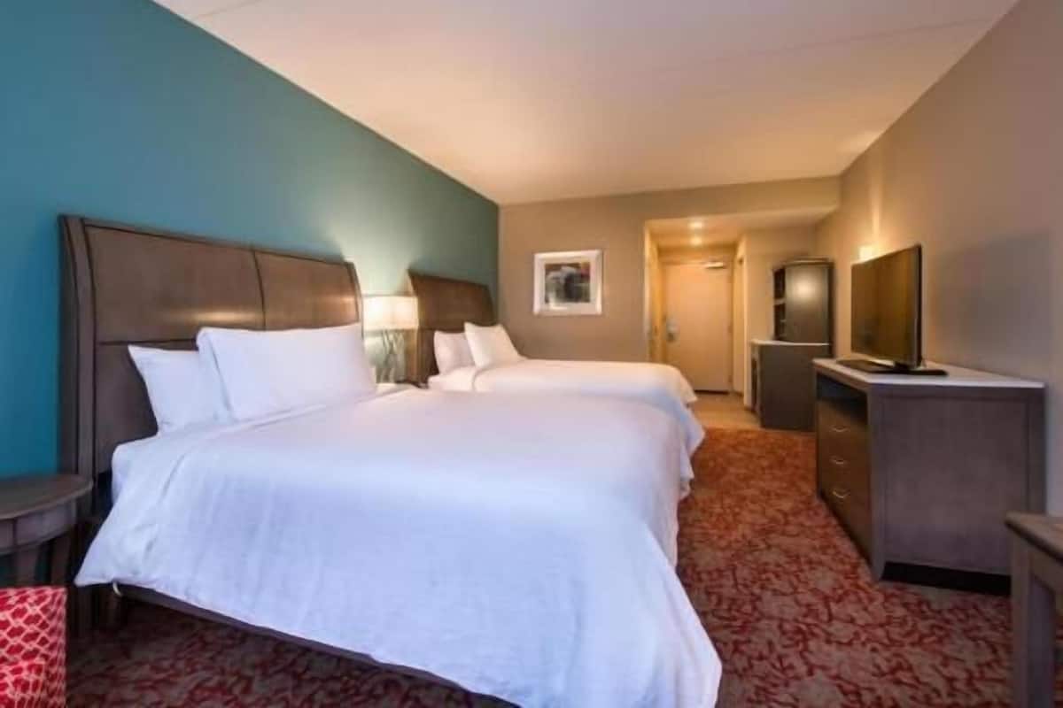 A hotel room with two beds, a desk, a TV, and a wardrobe.