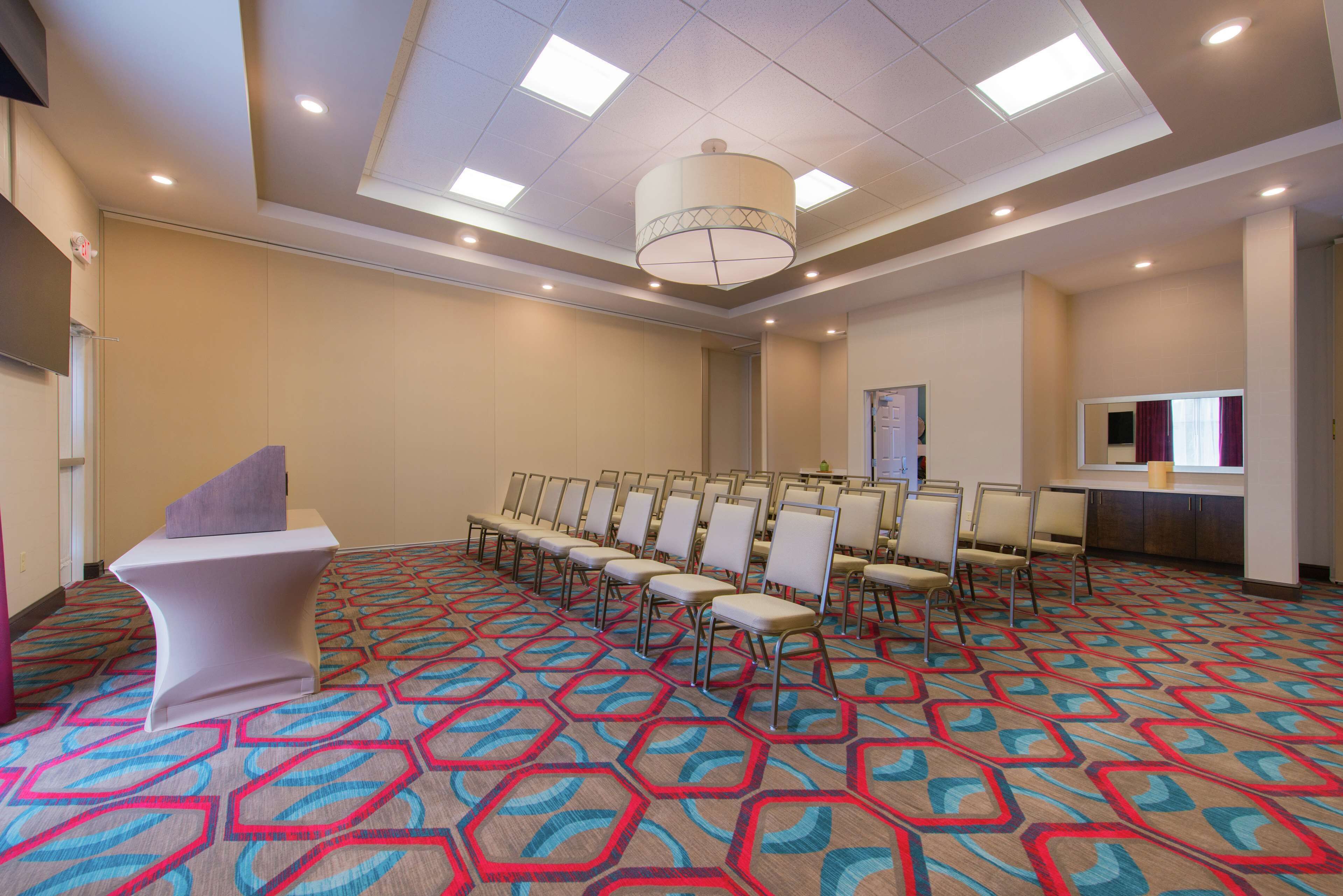 Une salle de conférence dotée d’un tapis à motifs, d’un pupitre blanc et de rangées de chaises.