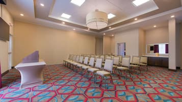 Une salle de conférence dotée d’un tapis à motifs, d’un pupitre blanc et de rangées de chaises.