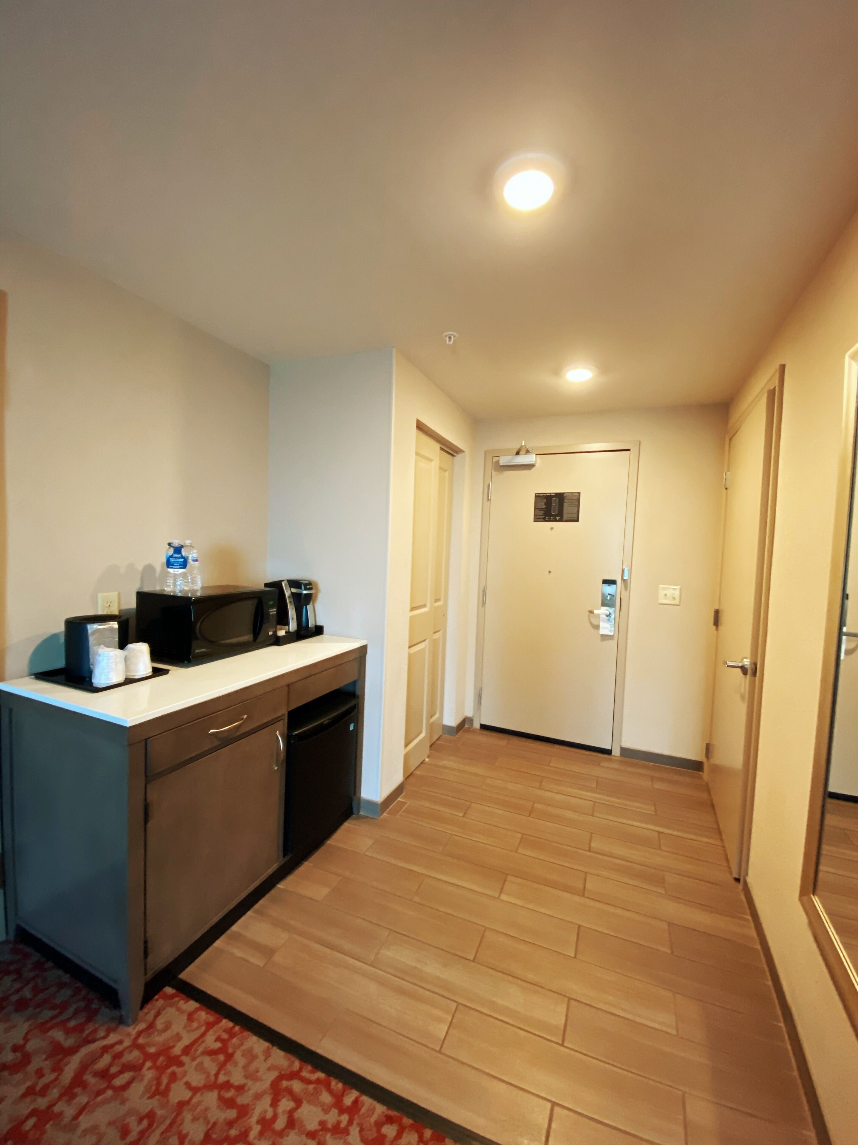 Habitación de hotel con kitchenette, piso de madera y puerta con cerradura.