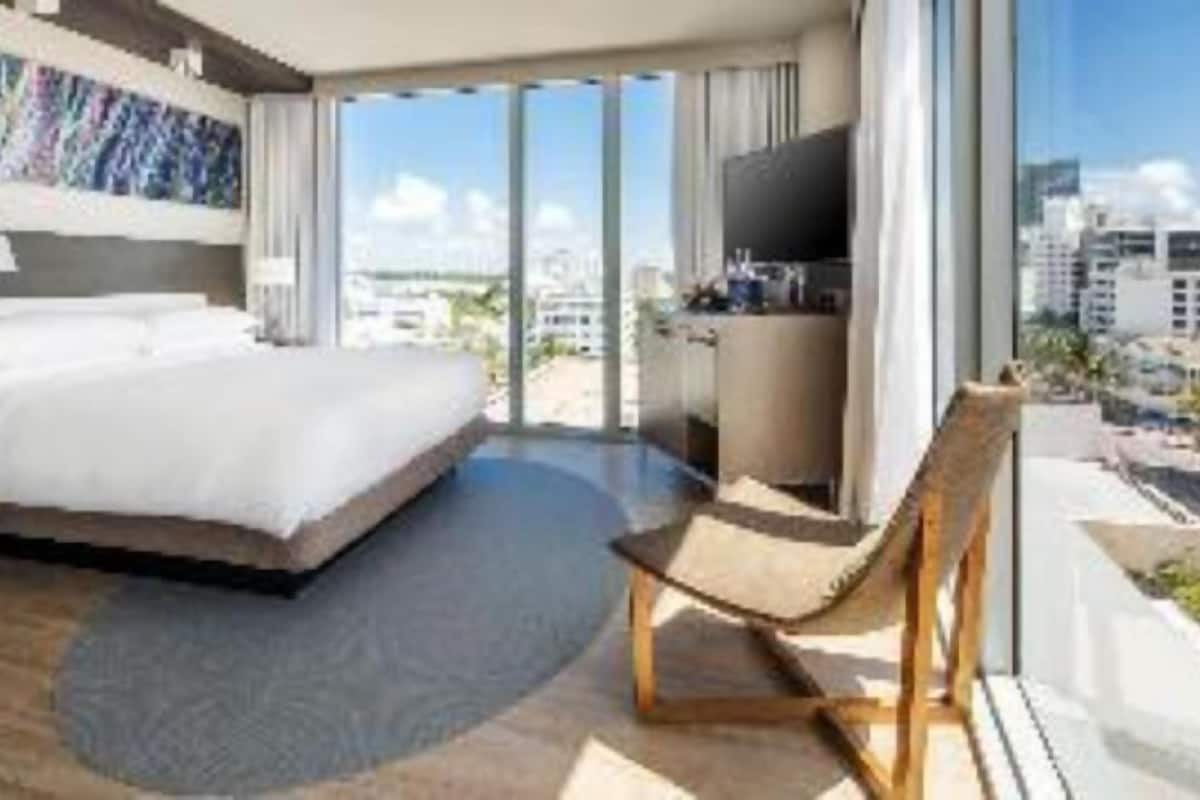 Una habitación de hotel moderna con una cama grande, un escritorio, un televisor y un balcón con vistas a la ciudad.