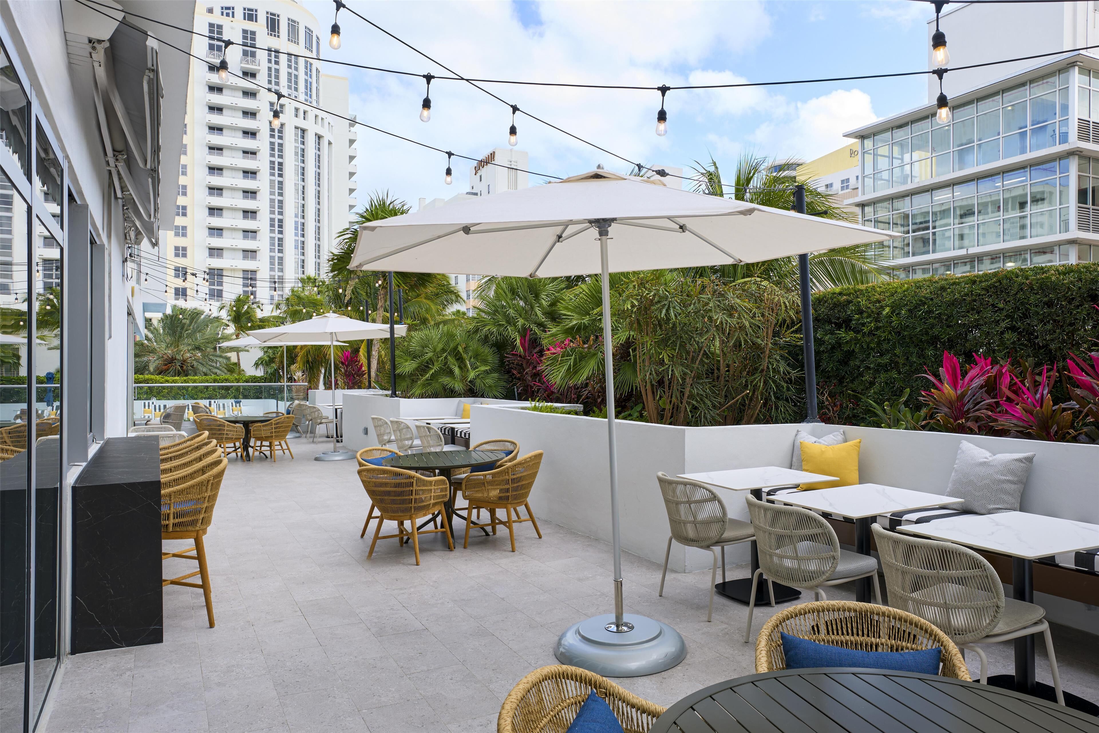 An outdoor patio with wicker furniture, umbrellas, and a view of tall buildings.