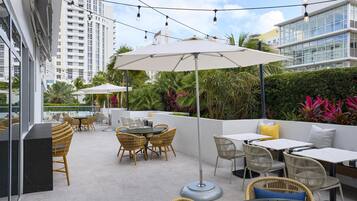 An outdoor patio with wicker furniture, umbrellas, and a view of tall buildings.