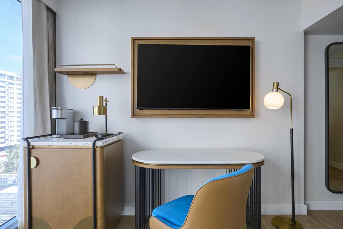 Habitación de hotel moderna con escritorio, silla y un ventanal con vistas a la ciudad.